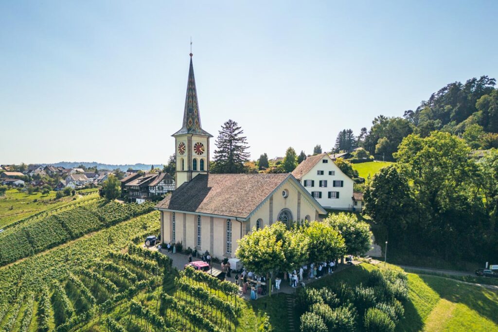 Drohnenfotografie einer Hochzeit in der Schweiz – Kirche im Weinberg Drohnenaufnahme einer Hochzeitsgesellschaft bei einer Kirche inmitten von Weinbergen in der Schweiz – fotografiert von Christian Meixner.